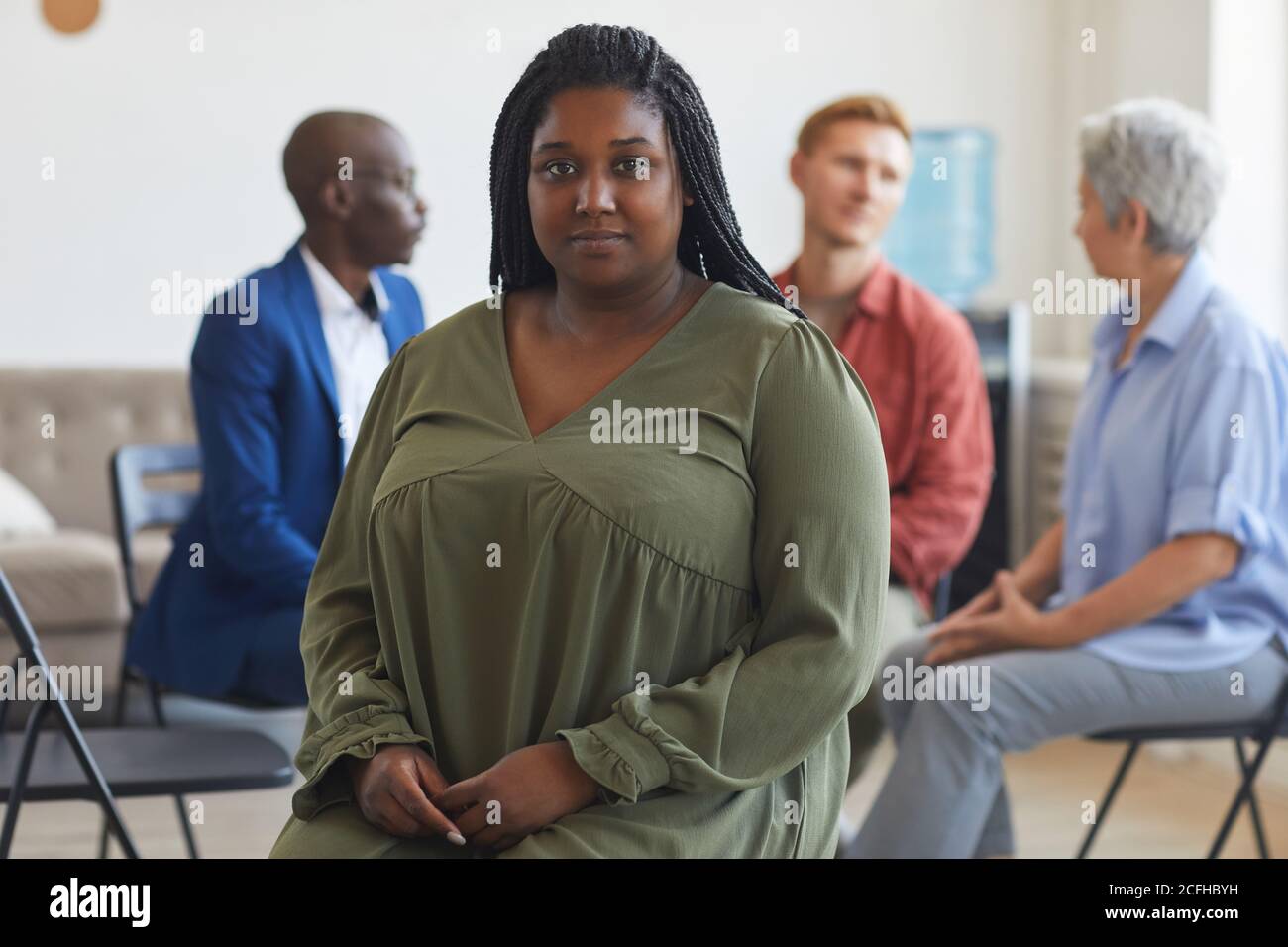 Portrait d'une jeune femme afro-américaine regardant la caméra lors d'une réunion de groupe de soutien avec des personnes assises en cercle en arrière-plan, espace de copie Banque D'Images