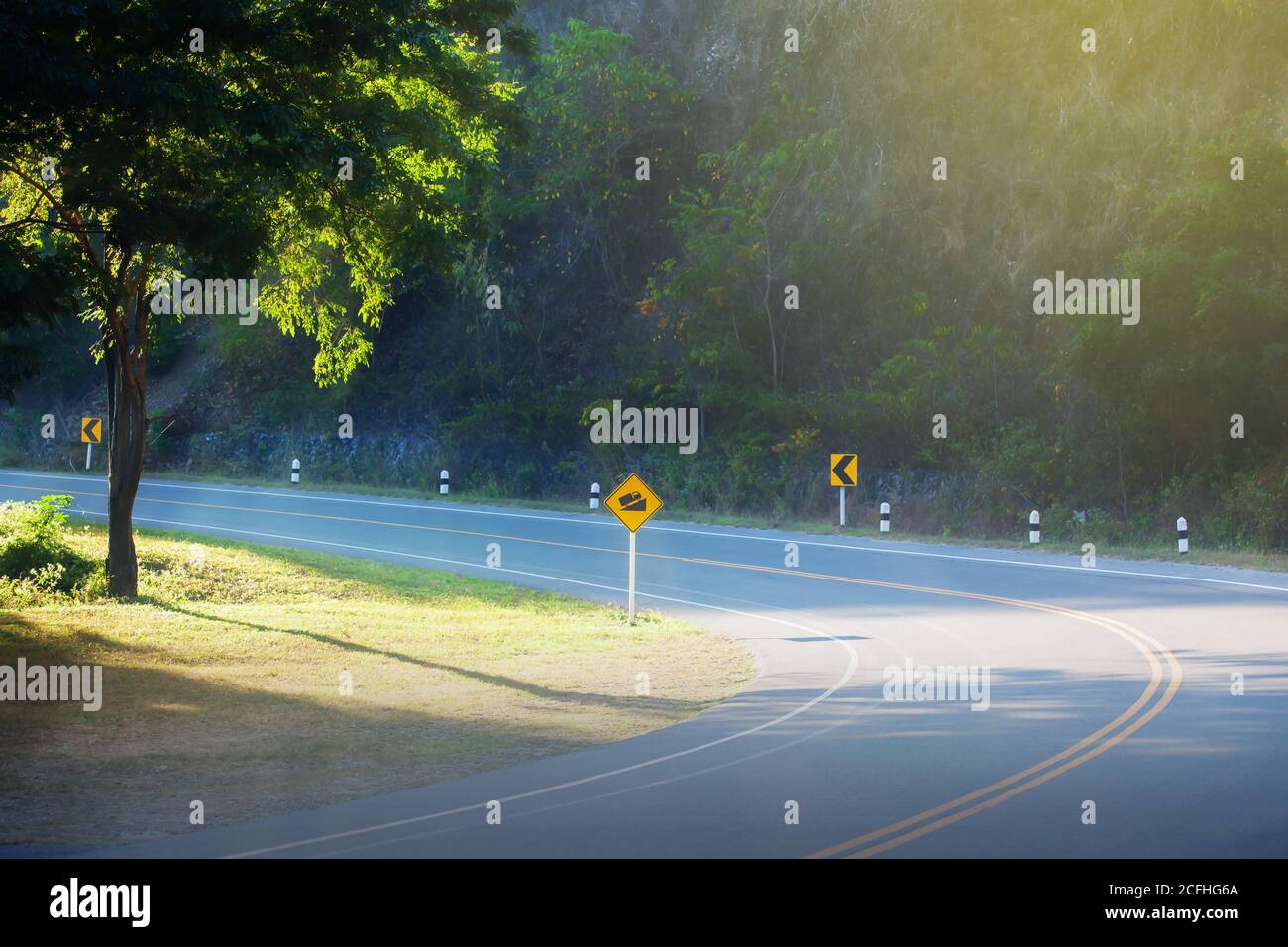 Une route forestière courbe vide et des panneaux d'avertissement de route jaune au lever du soleil. Concentrez-vous sur la route asphaltée. Banque D'Images