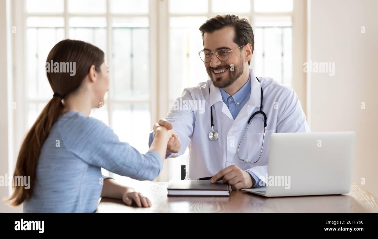 Jeune médecin souriant portant une main de patient femelle uniforme secouée Banque D'Images