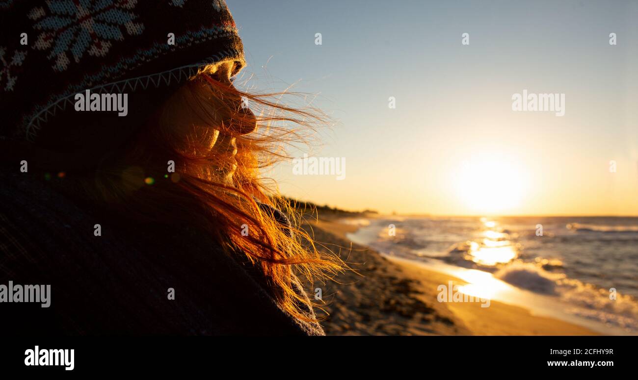 Une femme voyageur regarde la mer au lever du soleil. Ses cheveux se délèrent dans le vent Banque D'Images