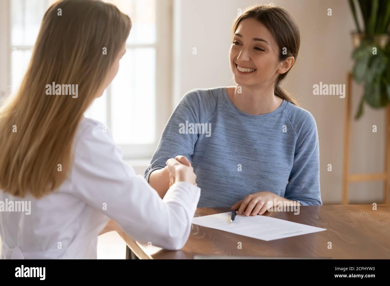 Jeune femme souriante qui secoue la main du médecin, signant le contrat d'assurance médicale Banque D'Images