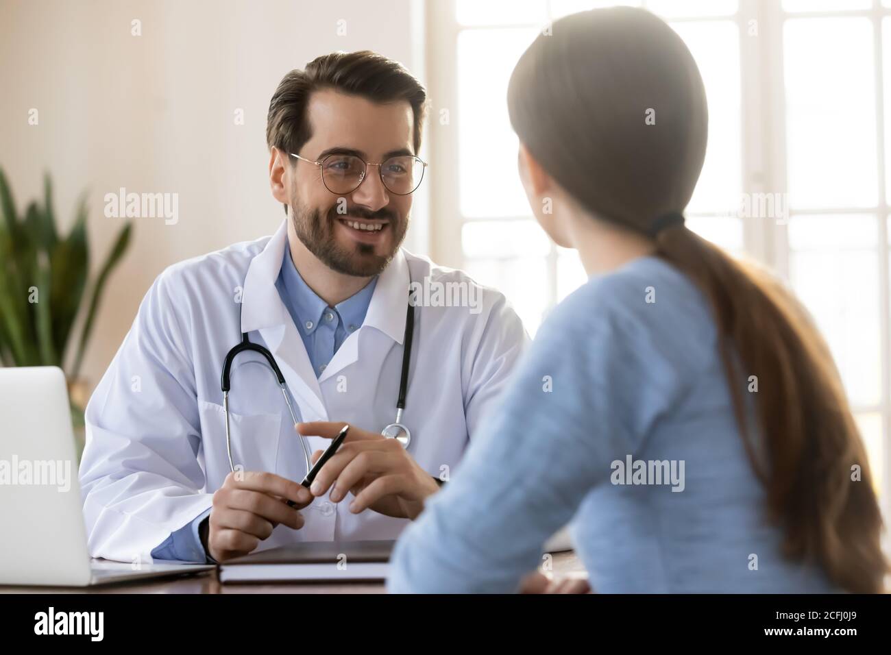 Jeune médecin thérapeute souriant à l'écoute des plaintes des patients lors de la réunion Banque D'Images
