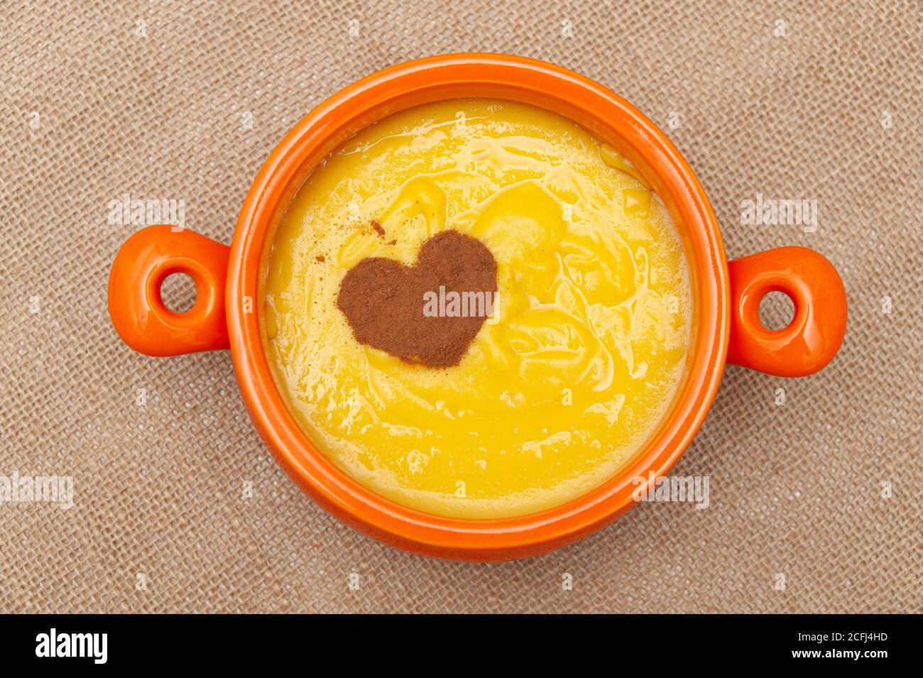 Pudding au maïs sucré fait maison connu au Brésil sous le nom de Curau ou Canjica Nordestina dans un bol en céramique. Cannelle en poudre en forme de coeur. Banque D'Images