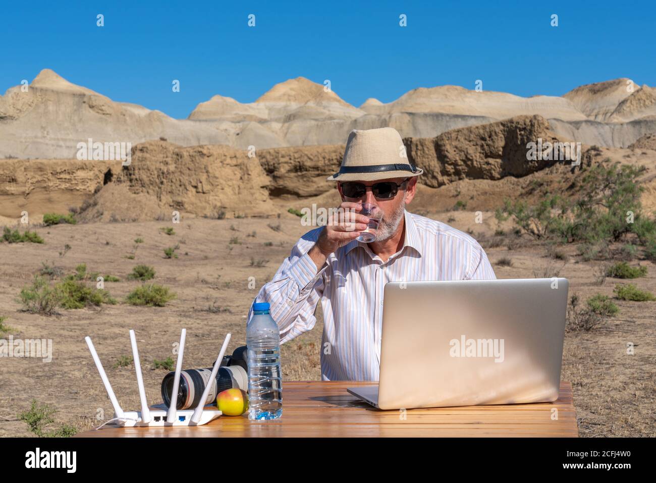 Un homme travaille à l'extérieur sur un ordinateur portable par temps chaud et boissons de l'eau d'un verre Banque D'Images