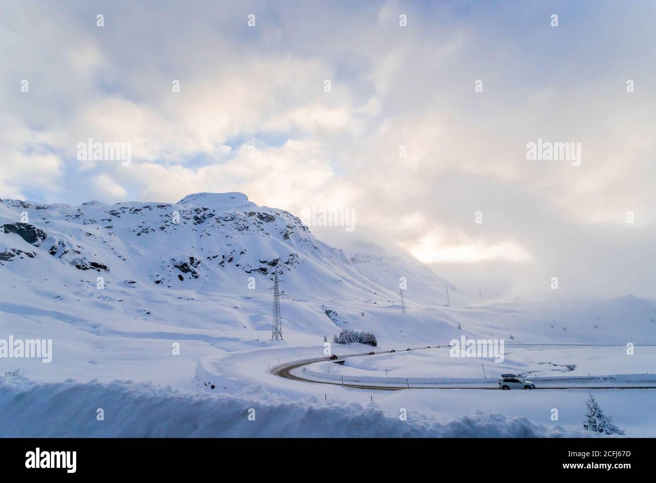 Hiver la neige couvre les montagnes et la route en Suisse avec l'arrière-plan de beau soleil de soirée et de nuages spectaculaires Banque D'Images