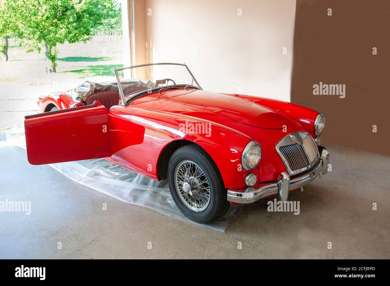 belle voiture de sport en haut en rouge vif sur un tarpe en plastique dans le garage de quelqu'un qui a été beaucoup aimé Banque D'Images