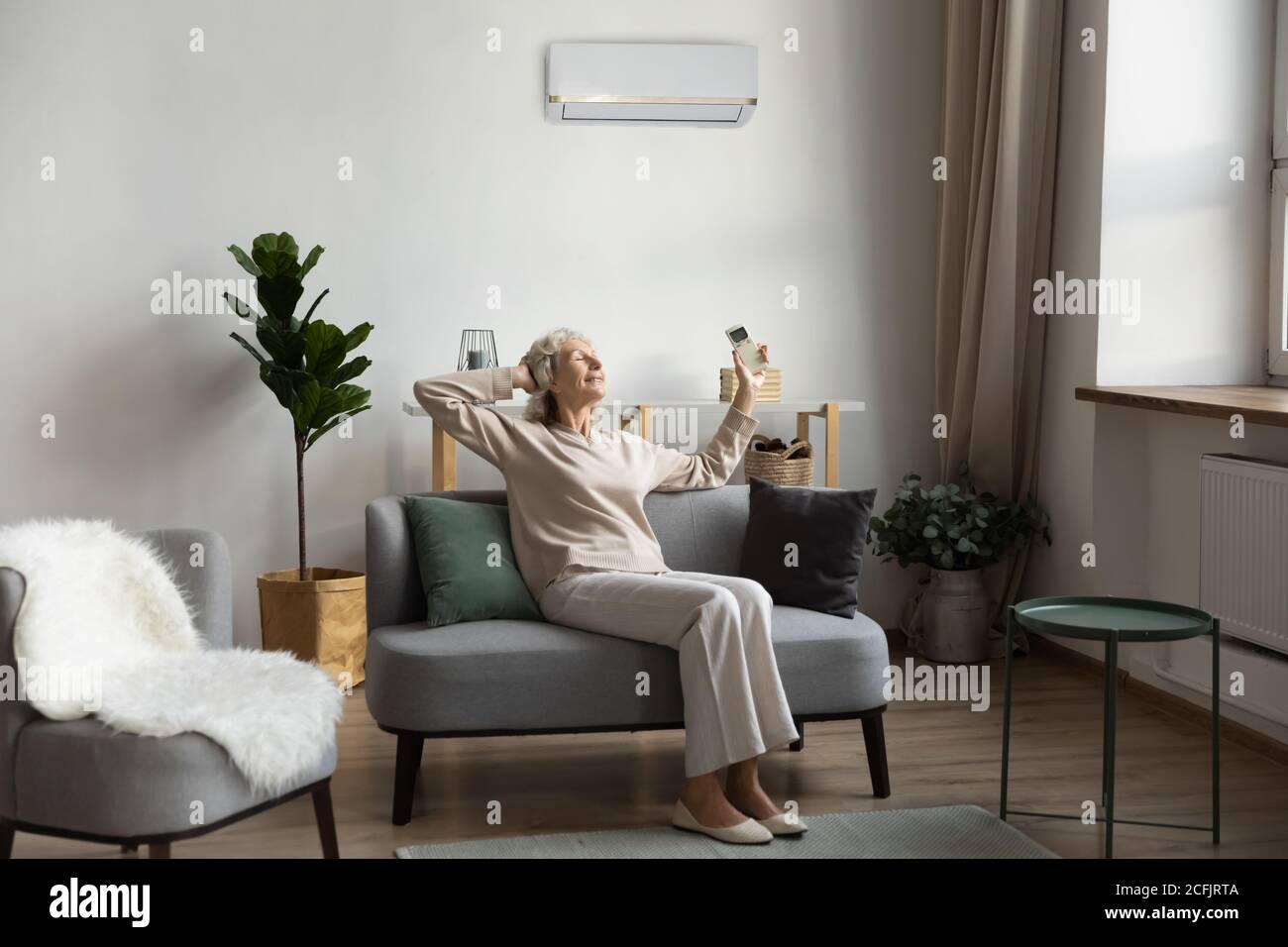 Femme plus souriante tenant la télécommande de climatisation, se détendre Banque D'Images