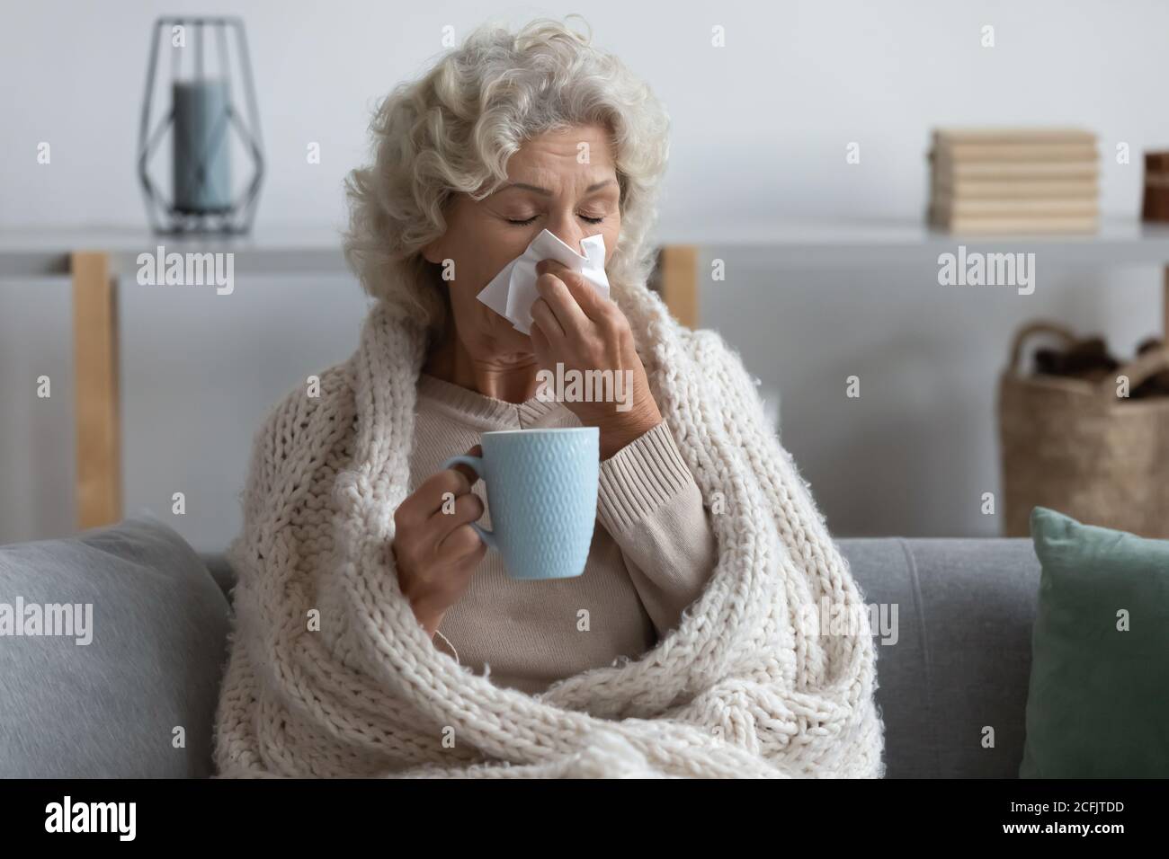 Malade mature femme enveloppée couverture soufflant nez de course, se sentant malsain Banque D'Images