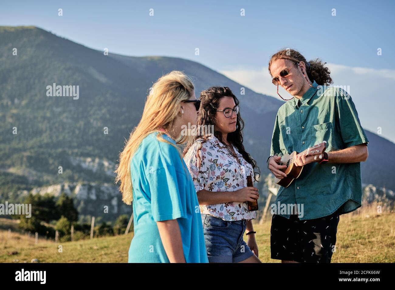 Des gens chaleureux et gais jouant ukulele tout en divertissant pendant le week-end été et debout sur l'herbe dans les hautes terres Banque D'Images