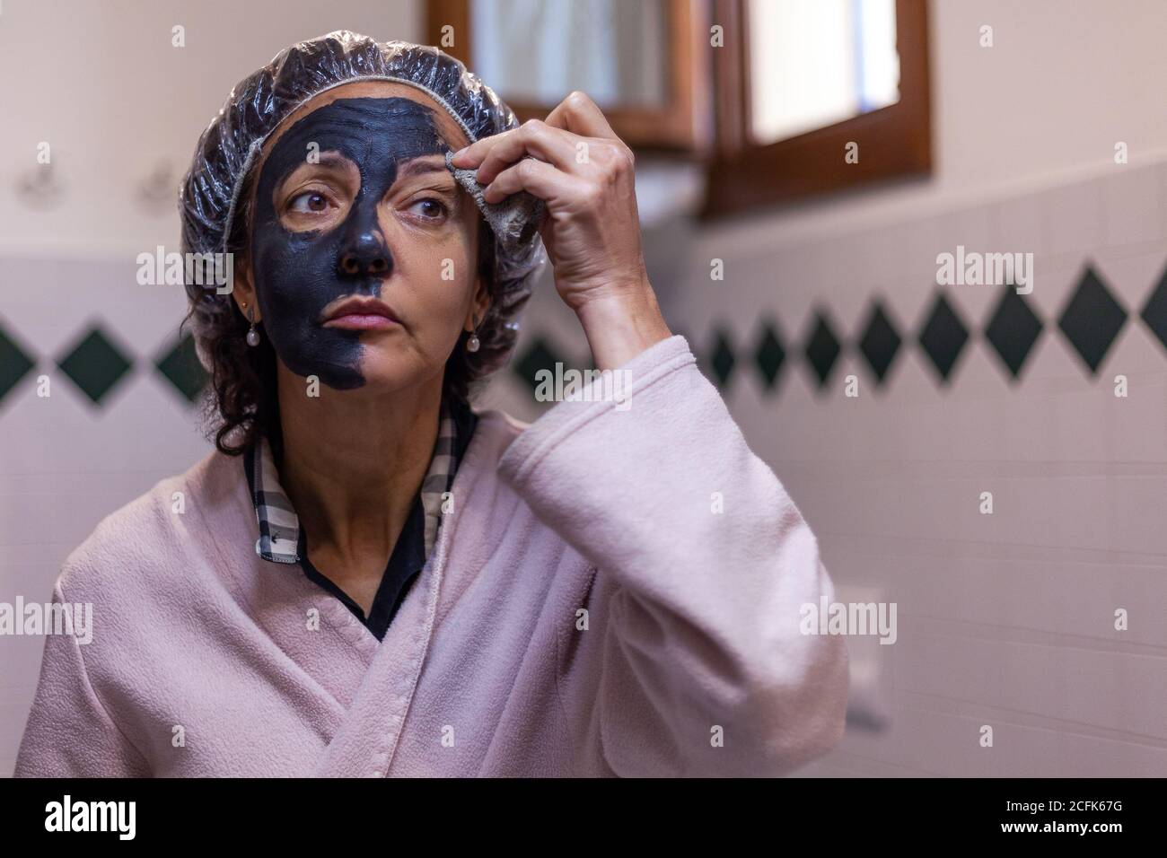 Femme dans une salle de bains prenant le masque de boue sur l'oeil avec éponge Banque D'Images
