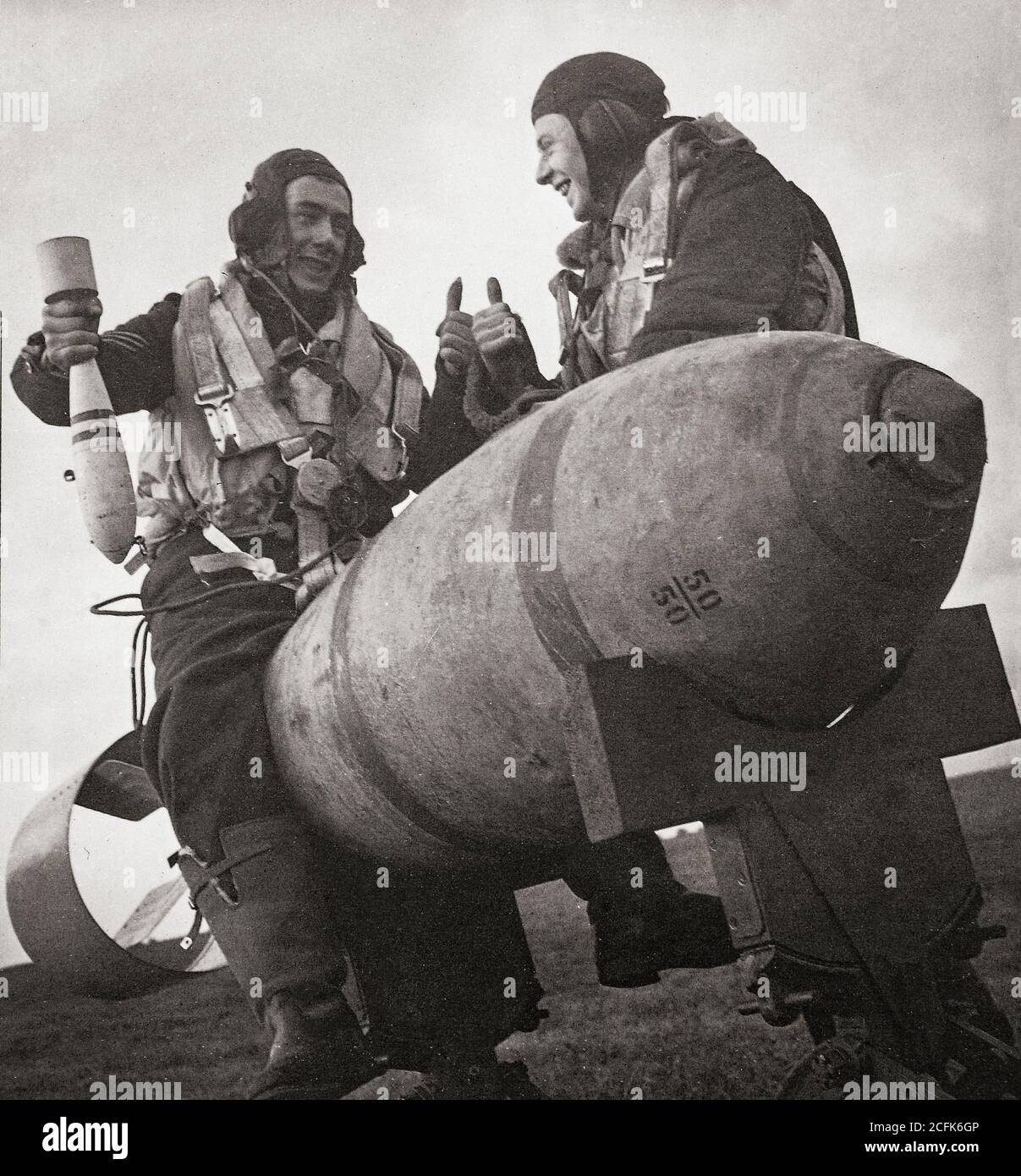 Un pilote est assis sur une bombe à usage général de 1,000 kg, la plus grande disponible en 1941, en train de jouer avec une bombe d'entraînement de 11 kg et demi, tout en discutant avec d'autres membres de l'équipage Banque D'Images