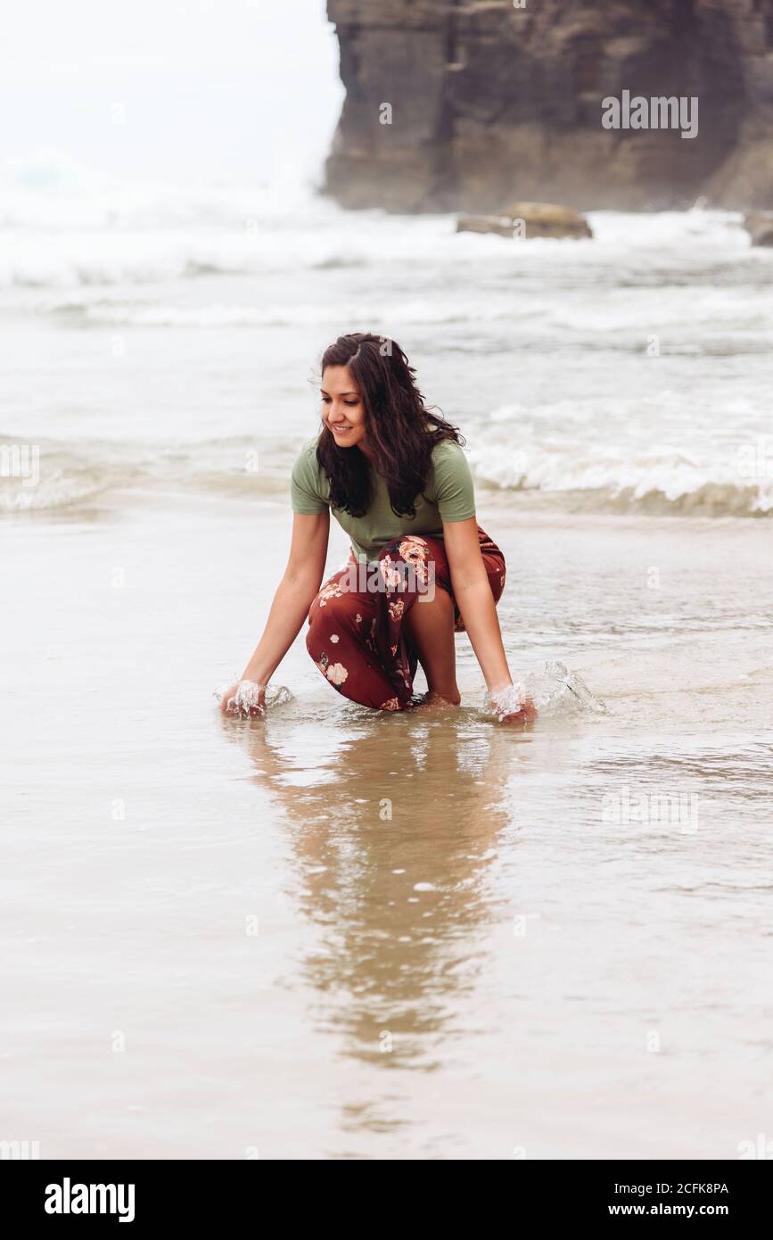 Une femme ravie, vêque de vêtements mouillés, se promenant le long de la mer arrière-plan de la falaise rocheuse Banque D'Images