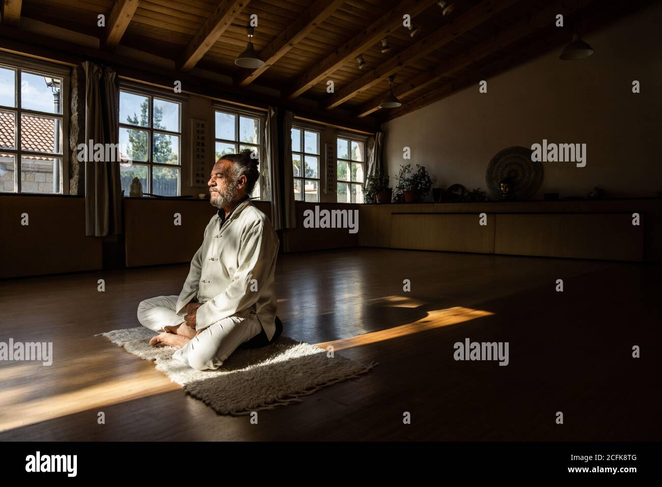 Vue latérale complète du corps d'un homme senior ethnique barbu pratiquer la méditation chi kung en position lotus dans un studio sombre Banque D'Images
