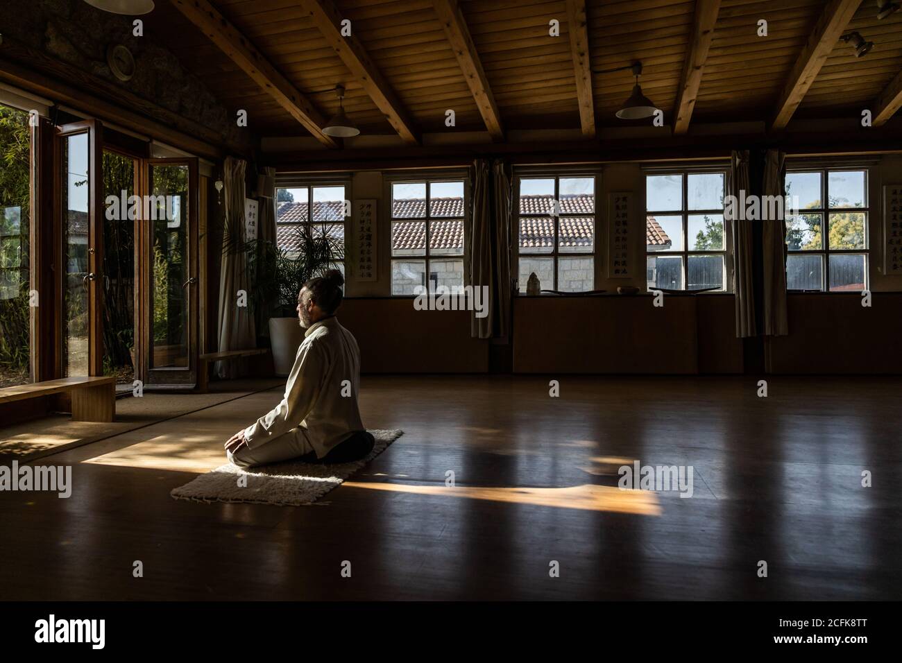 Vue latérale complète du corps d'un homme senior ethnique barbu pratiquer la méditation chi kung en position lotus dans un studio sombre Banque D'Images