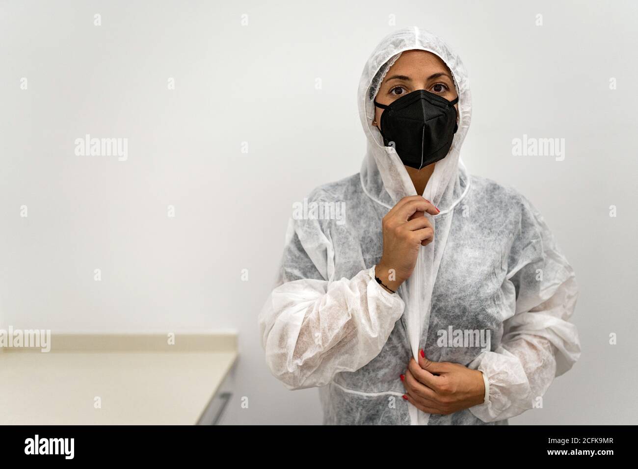 Femme médecin spécialiste en costume de protection avec masque et un capuchon protecteur lors de la préparation au travail pendant la pandémie du coronavirus Banque D'Images