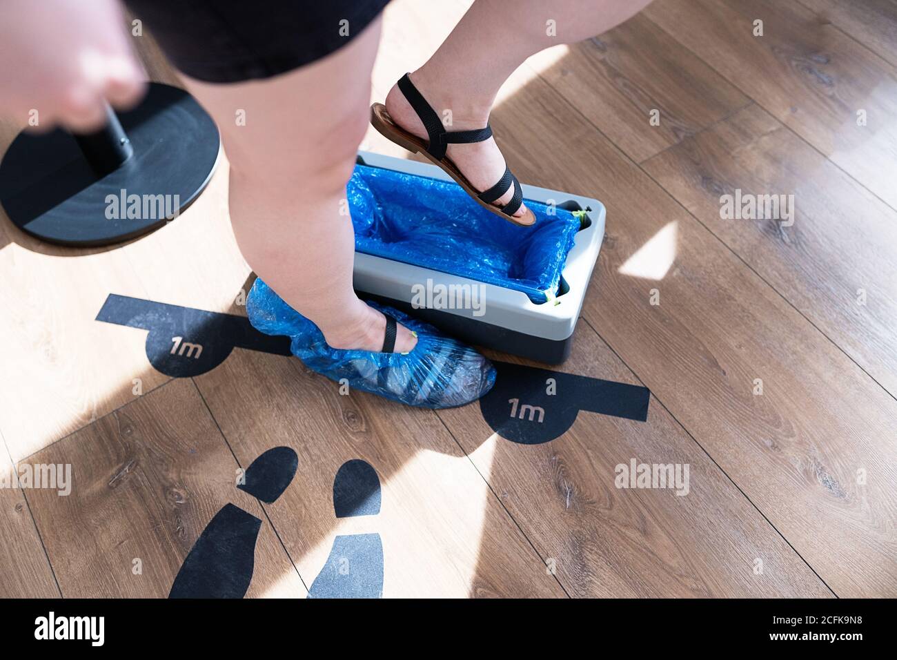 De dessus de crop anonyme visiteur de sexe féminin marche sur automatique dispositif pour surchaussures placé à l'entrée de la clinique Banque D'Images