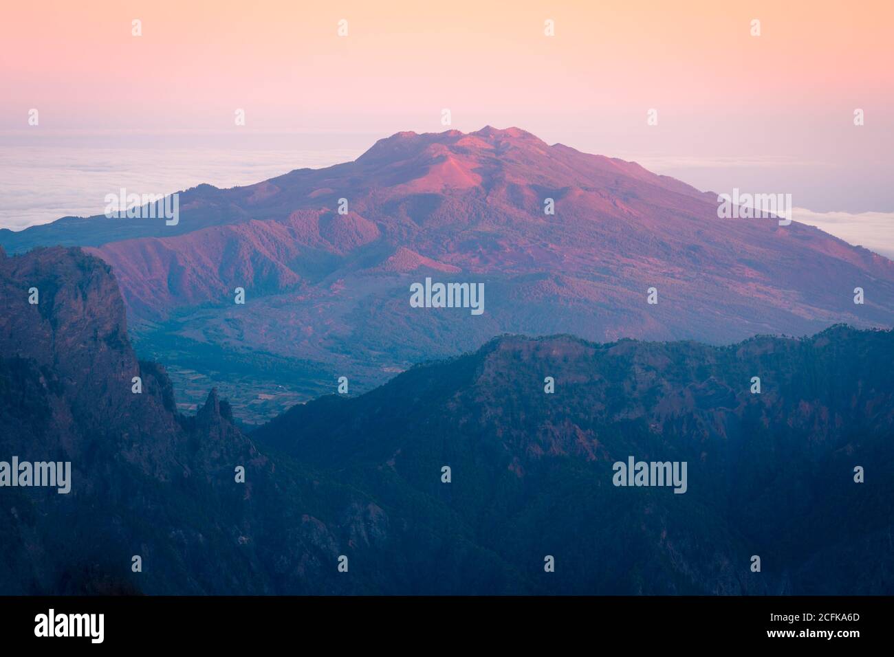 Paysage majestueux de la chaîne de montagnes couverte de nuages et de vallée avec des arbres sous un ciel bleu sans nuages Banque D'Images