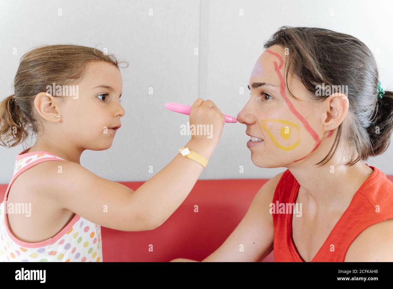Vue latérale de l'adorable petit enfant peint des photos sur le visage de mère tout en divertissant pendant le week-end à la maison Banque D'Images
