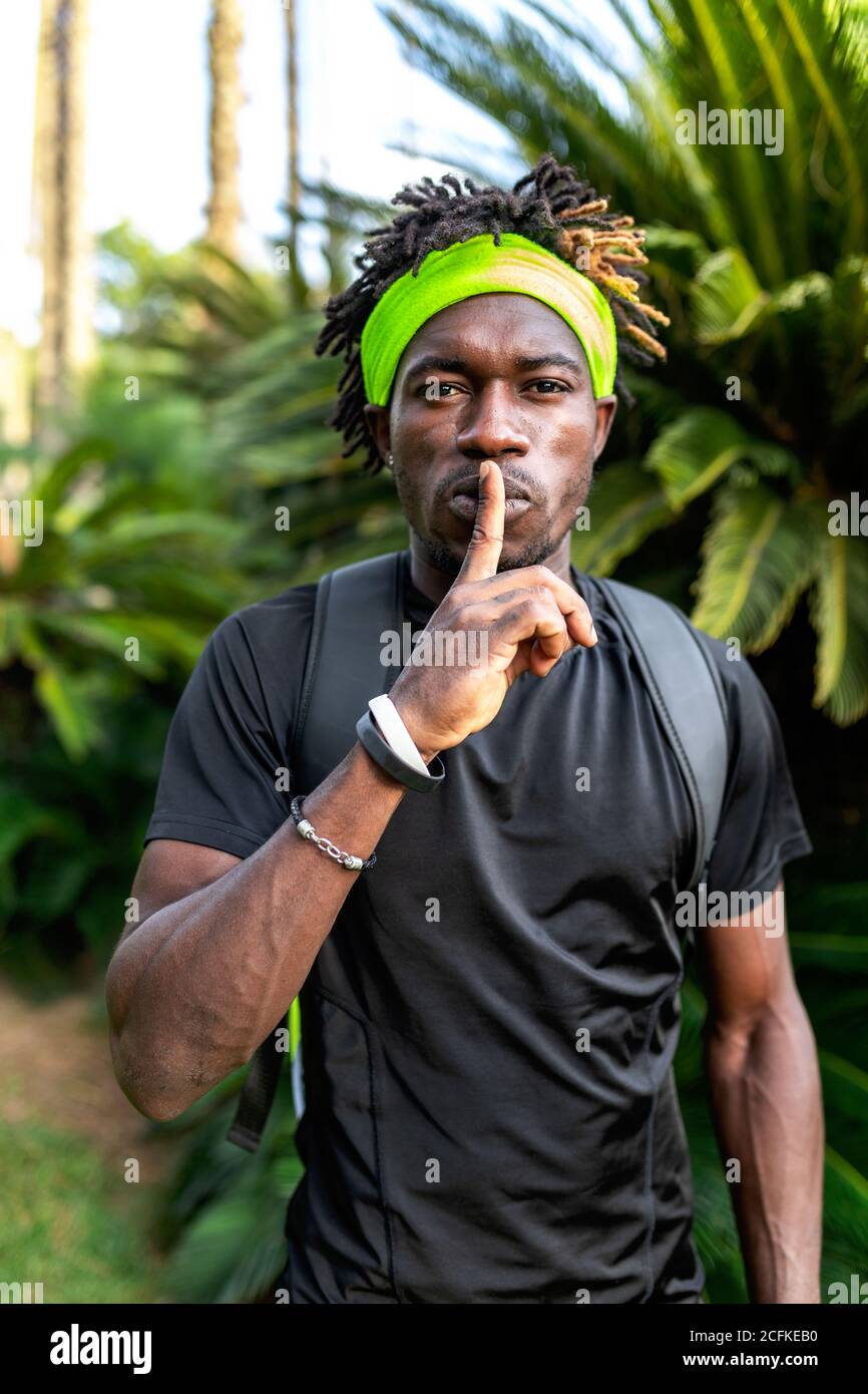 Jeune athlète afro-américain dans la fabrication de vêtements de sport et  de serre-tête shh geste tout en se tenant contre les plantes tropicales  vertes dans la rue Photo Stock - Alamy