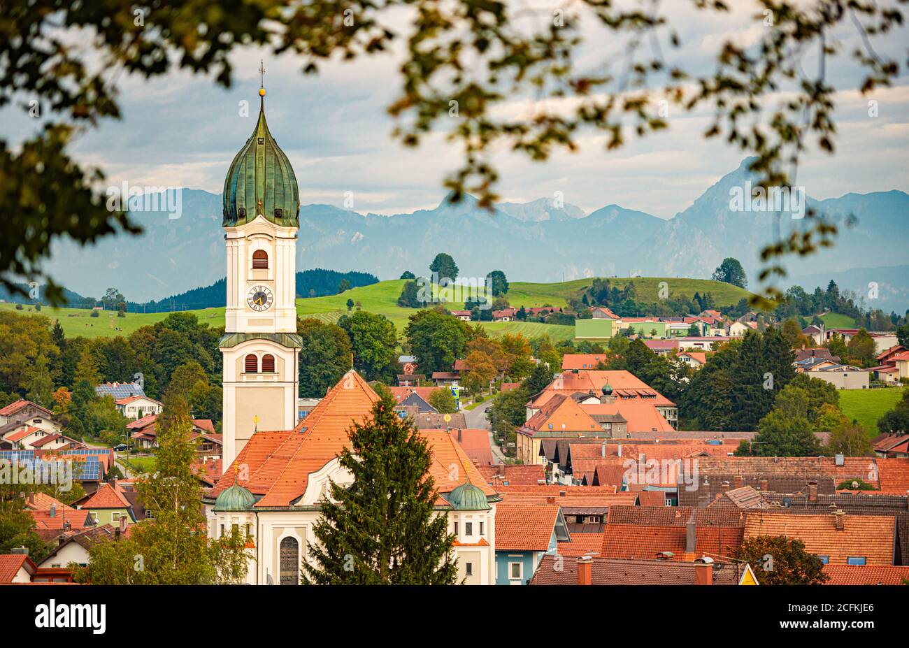 Beau et confortable petit village bavarois en Allemagne, en Europe. Église et maisons en premier plan avec ciel nuageux et montagnes en arrière-plan Banque D'Images