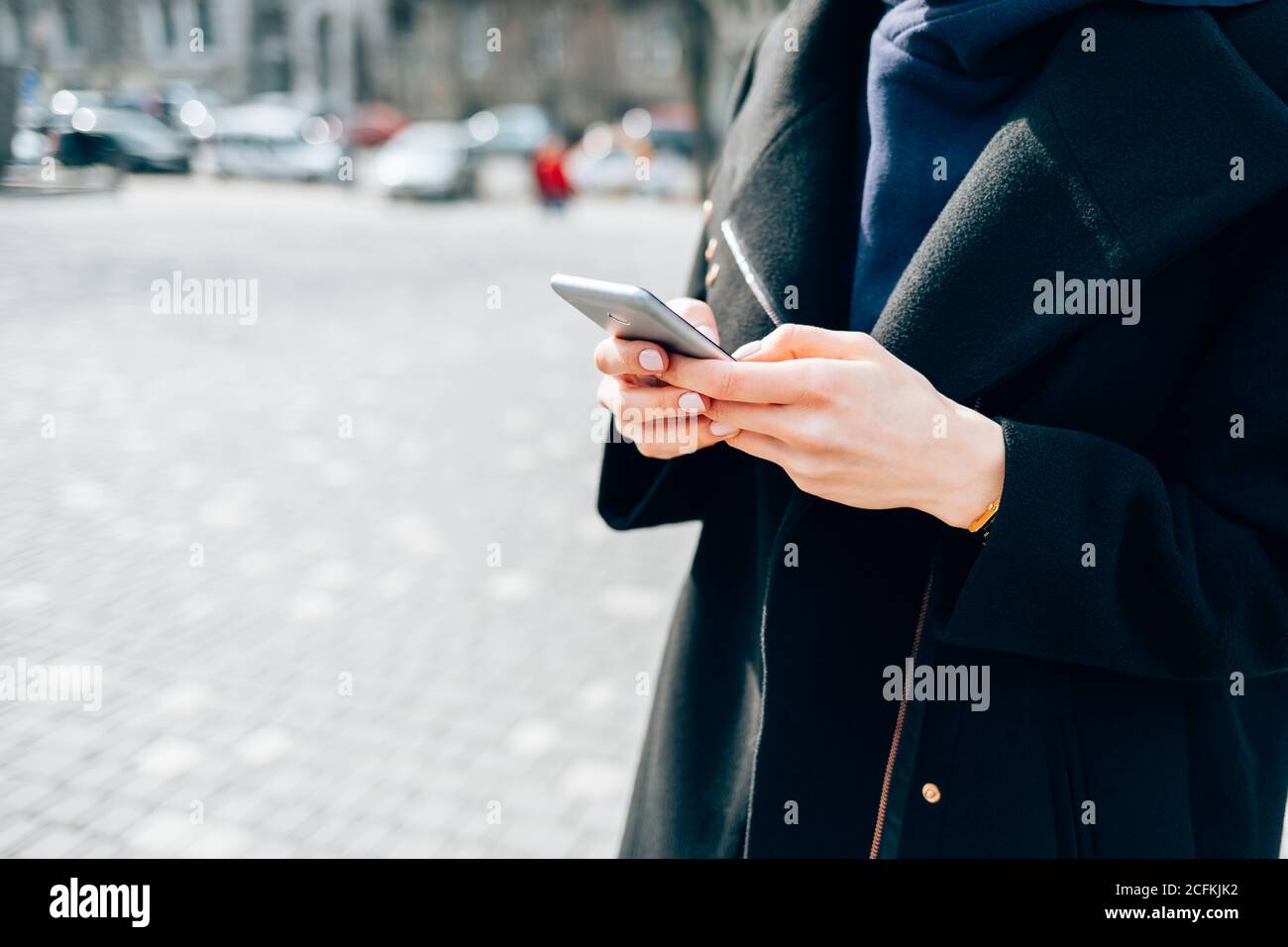 Femme portant un manteau noir avec un smartphone debout en ville le jour de l'automne Banque D'Images