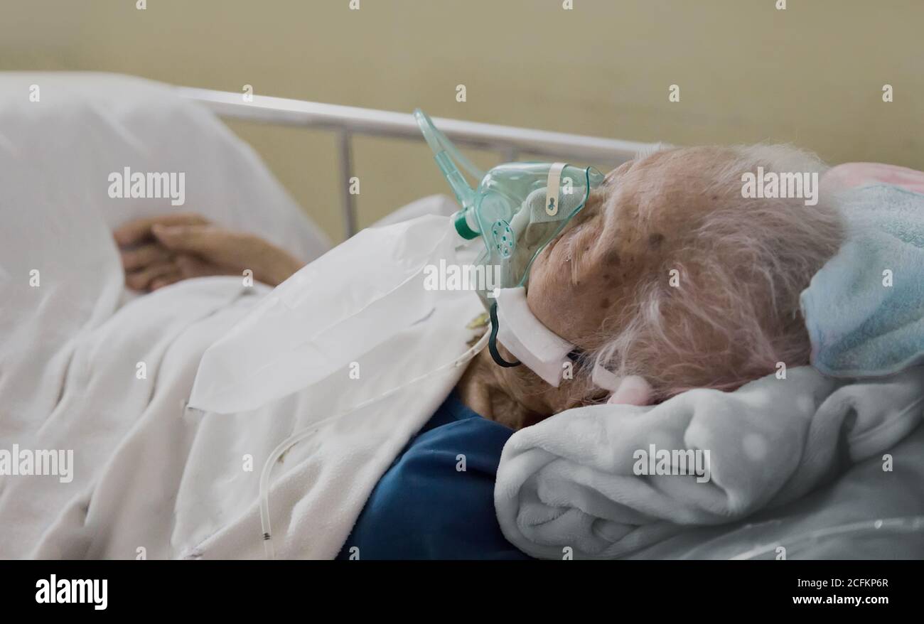 Processus de guérison pour la dernière brise de sécurité de vieux patient de femme à la retraite couchée dans un lit d'hôpital avec une goutte un masque et un équipement médical de fréquence cardiaque Banque D'Images
