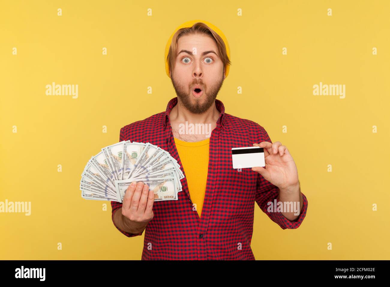 Épargne financière et commerce, prêt bancaire. Un gars hipster étonnant dans une chemise à carreaux tenant des factures de dollars et de carte de crédit, regardant la caméra choqué surpr Banque D'Images
