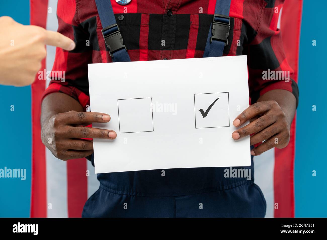 Jeune réparateur noir tenant le bulletin de vote avec une coche carrée Contre le drapeau américain Banque D'Images