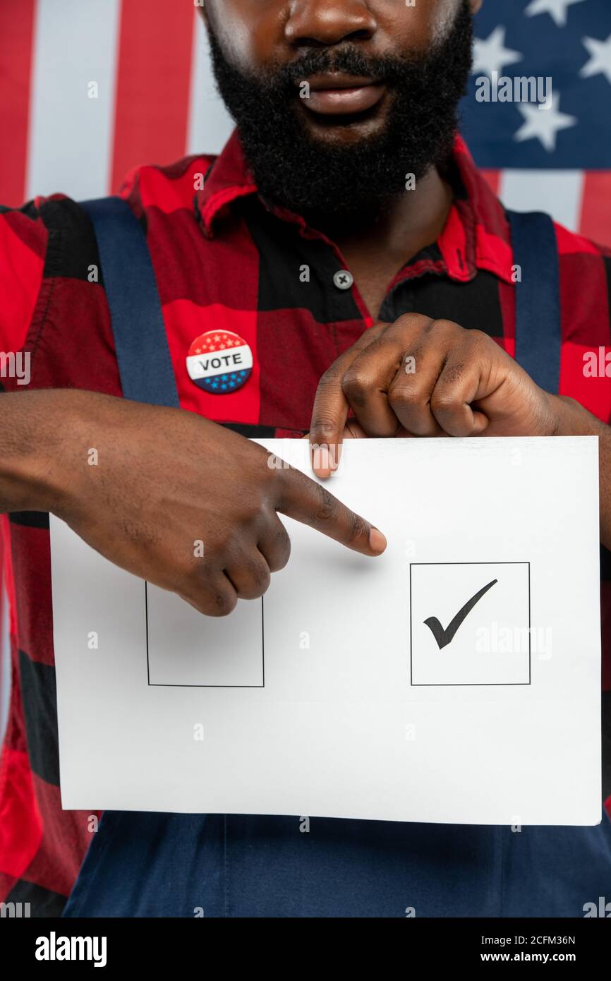 Main du jeune réparateur afro-américain qui pointe sur la coche sur le bulletin de vote papier Banque D'Images