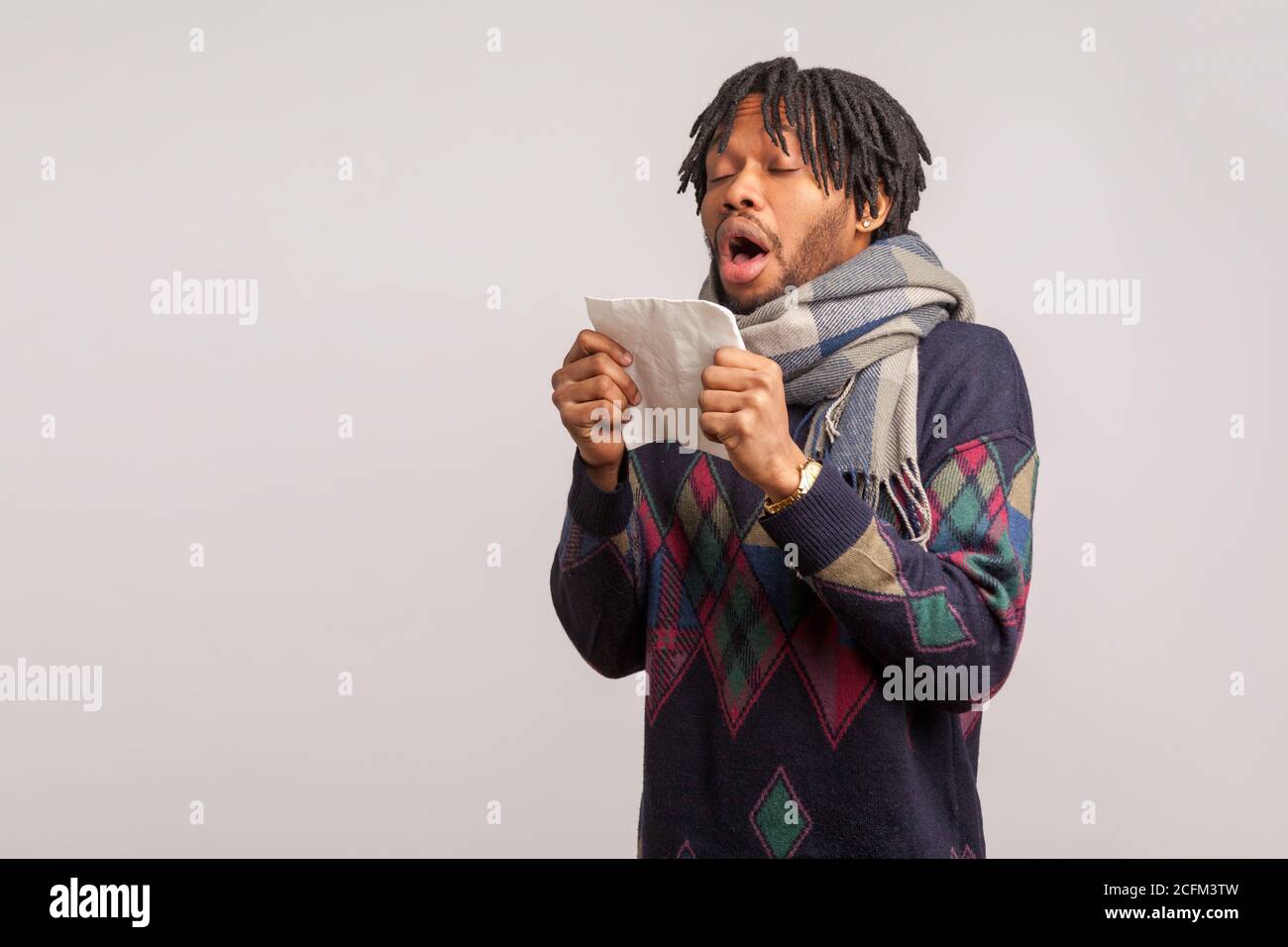 Bouleverser l'homme africain avec des dreadlocks dans le foulard à carreaux largement la bouche ouverte allant à éternuer, allergie saisonnière, la grippe. Prise de vue en studio isolée sur bac gris Banque D'Images