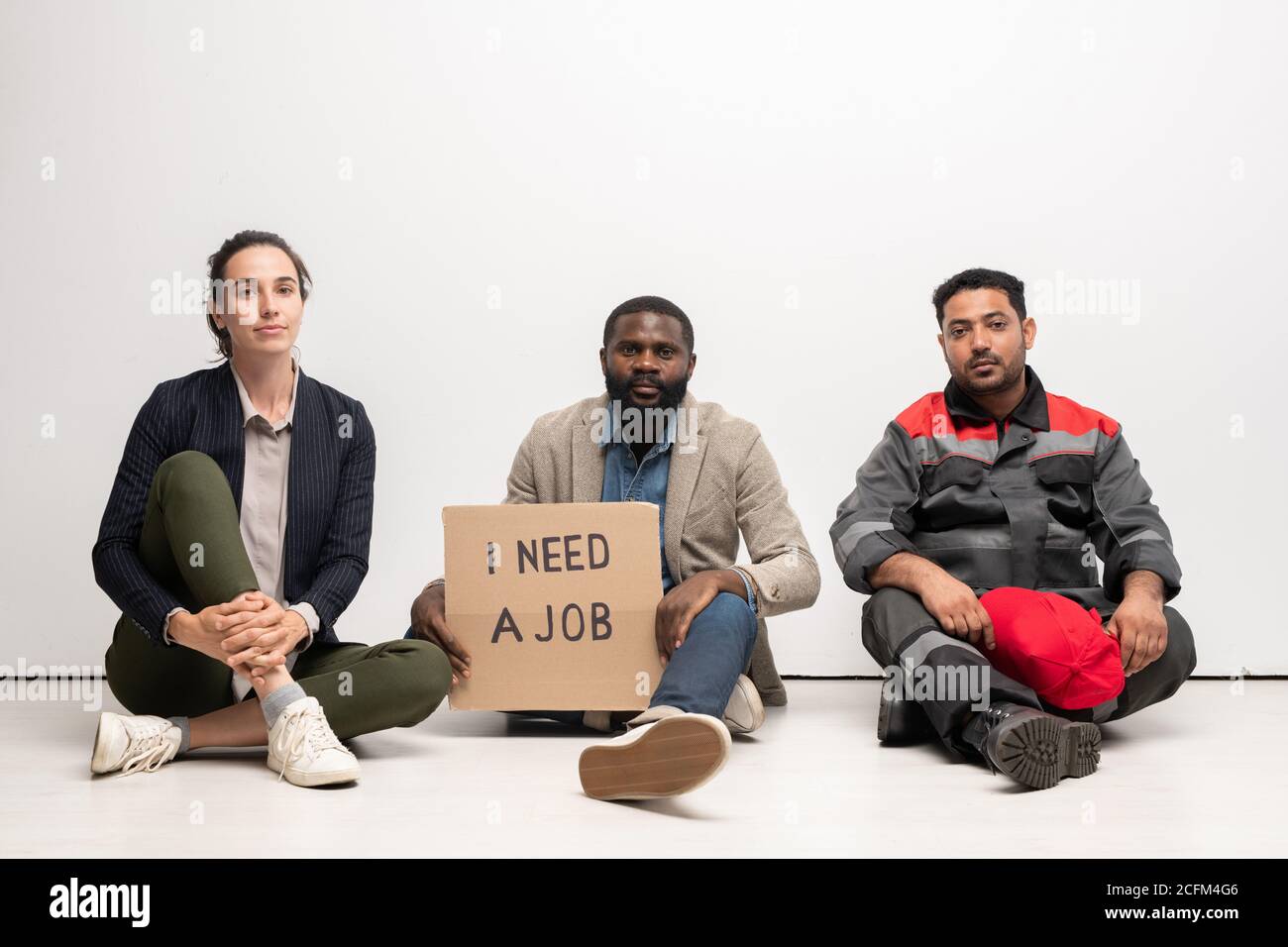 Groupe de jeunes interculturels sans emploi en vêtements décontractés assis le sol Banque D'Images