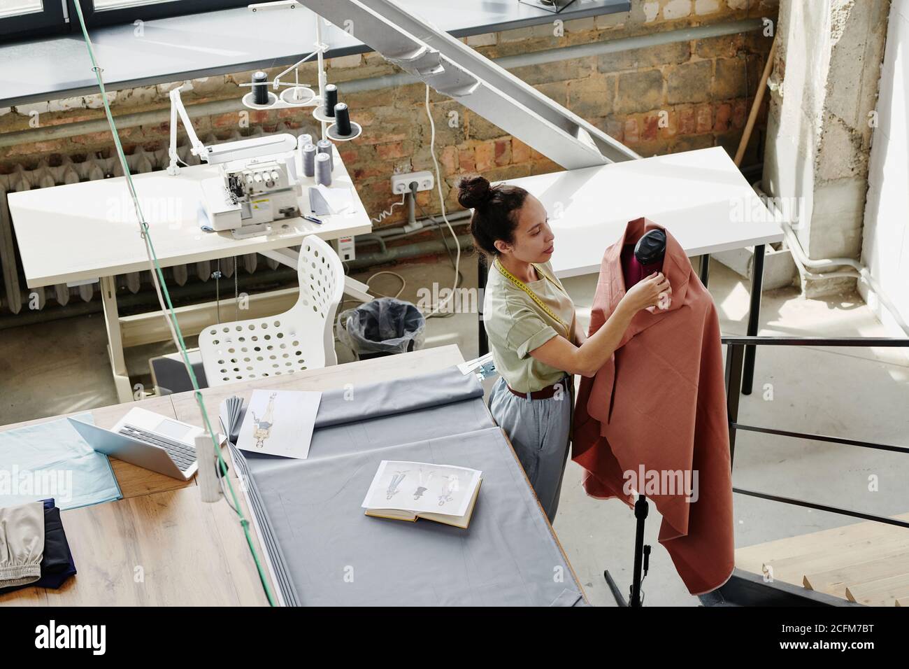 Jeune couturier travaillant avec du textile sur un mannequin debout par table Banque D'Images