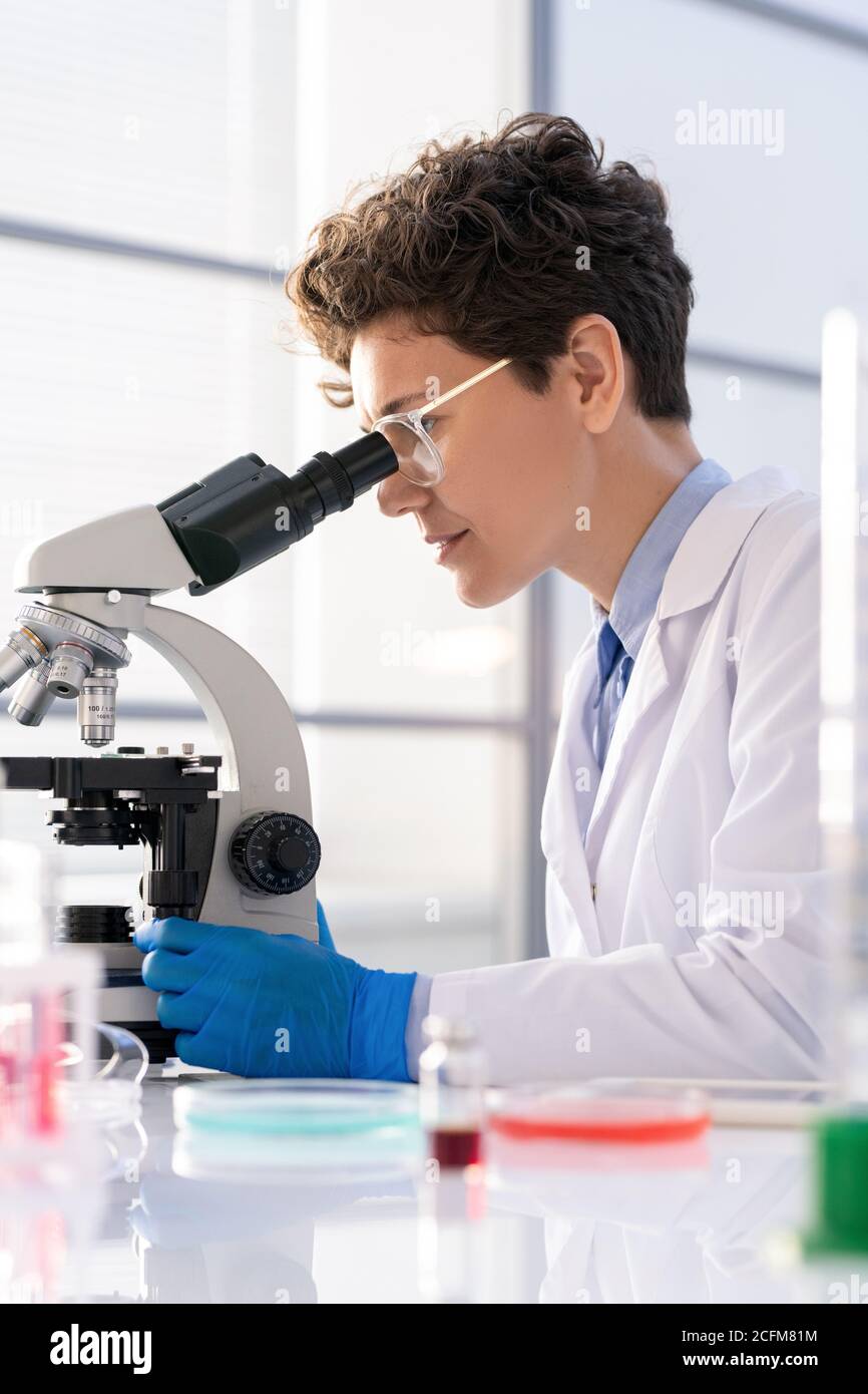 Jeune femme en whitecoat et gants de travail avec microscope dans laboratoire Banque D'Images