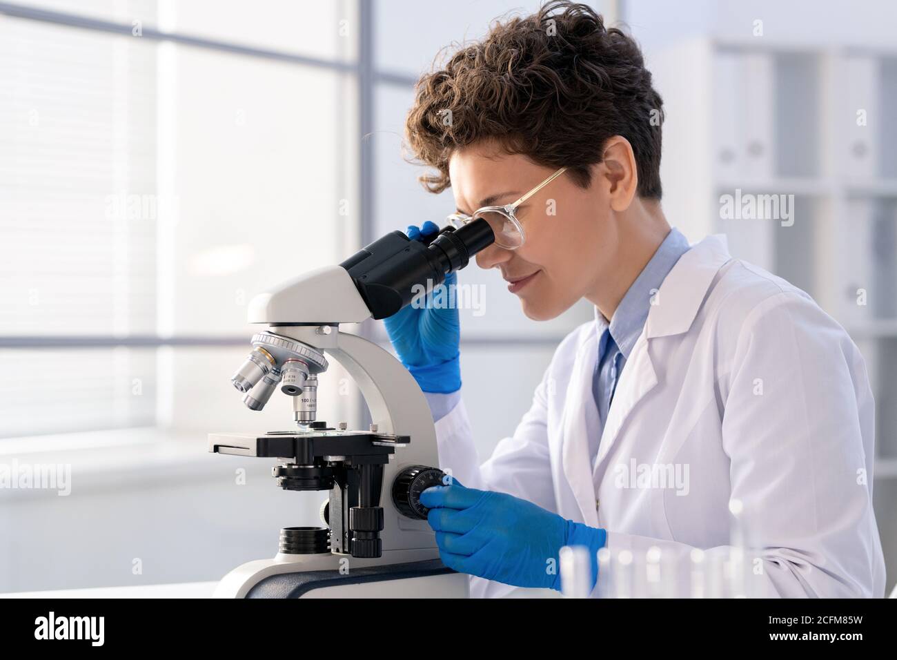 Jeune femme regardant au microscope tout en étudiant de nouvelles substances chimiques Banque D'Images