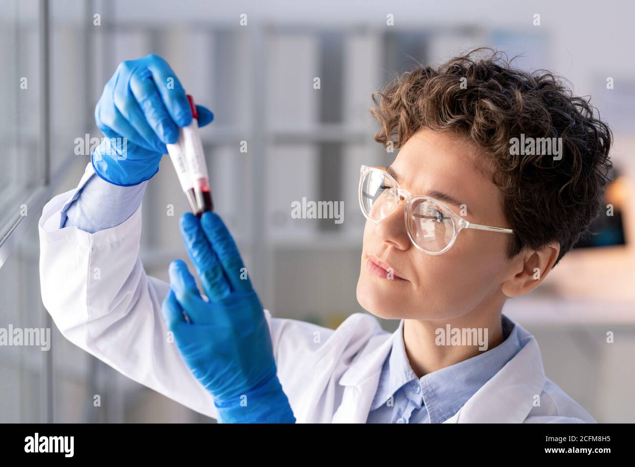 Un travailleur de laboratoire sérieux ganté qui regarde des flacons avec du sang de coronavirus tests Banque D'Images