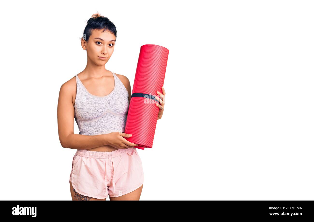 Jeune femme tenant un tapis de yoga attitude de pensée et d'expression sobre avoir l'air confiant Banque D'Images