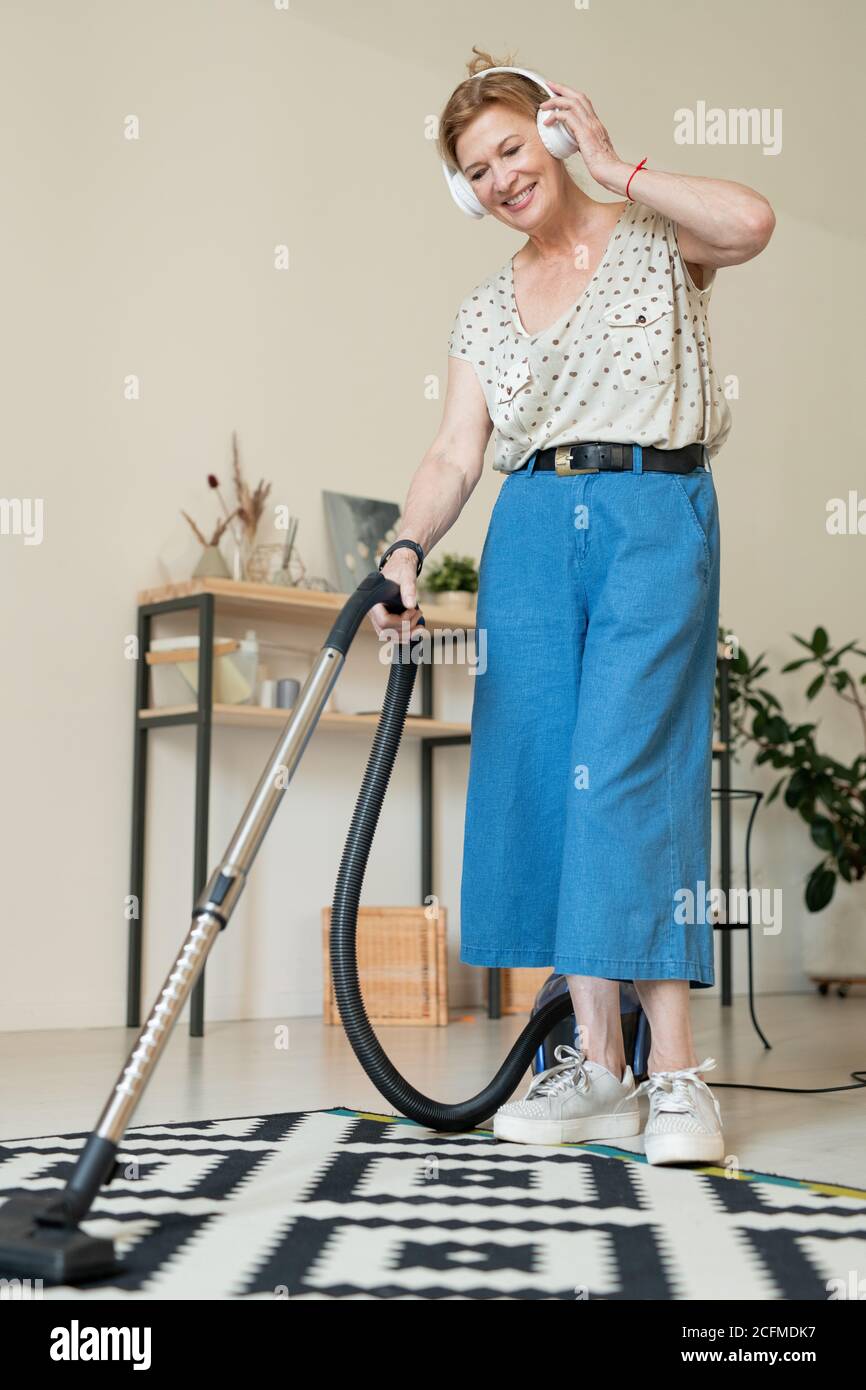 Femme d'intérieur gaie et mature en tenue décontractée, écoutant de la musique dans un casque Banque D'Images