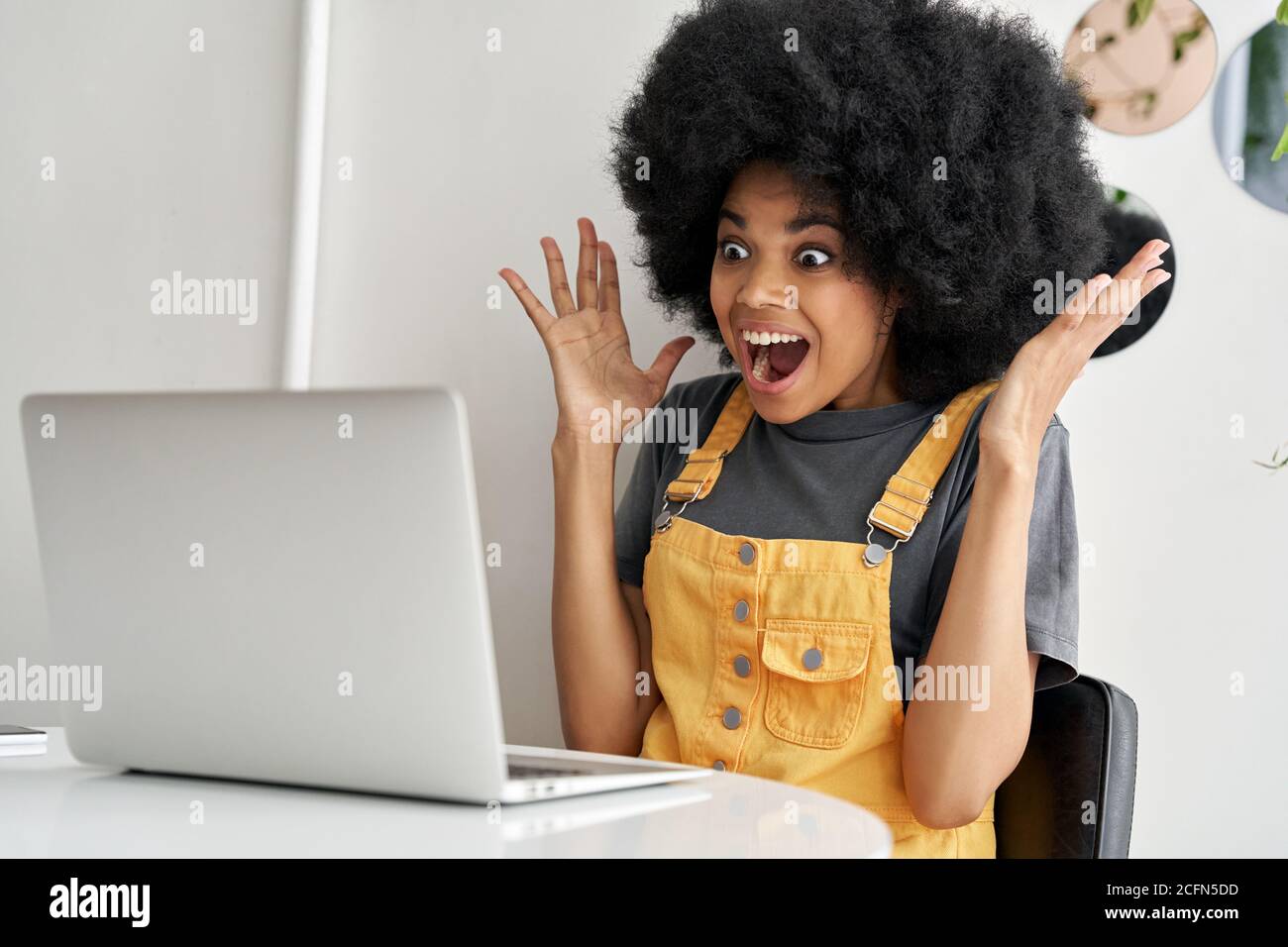 Une femme africaine excitée regardant le PC portable gagnant en ligne, lisant de grandes nouvelles. Banque D'Images