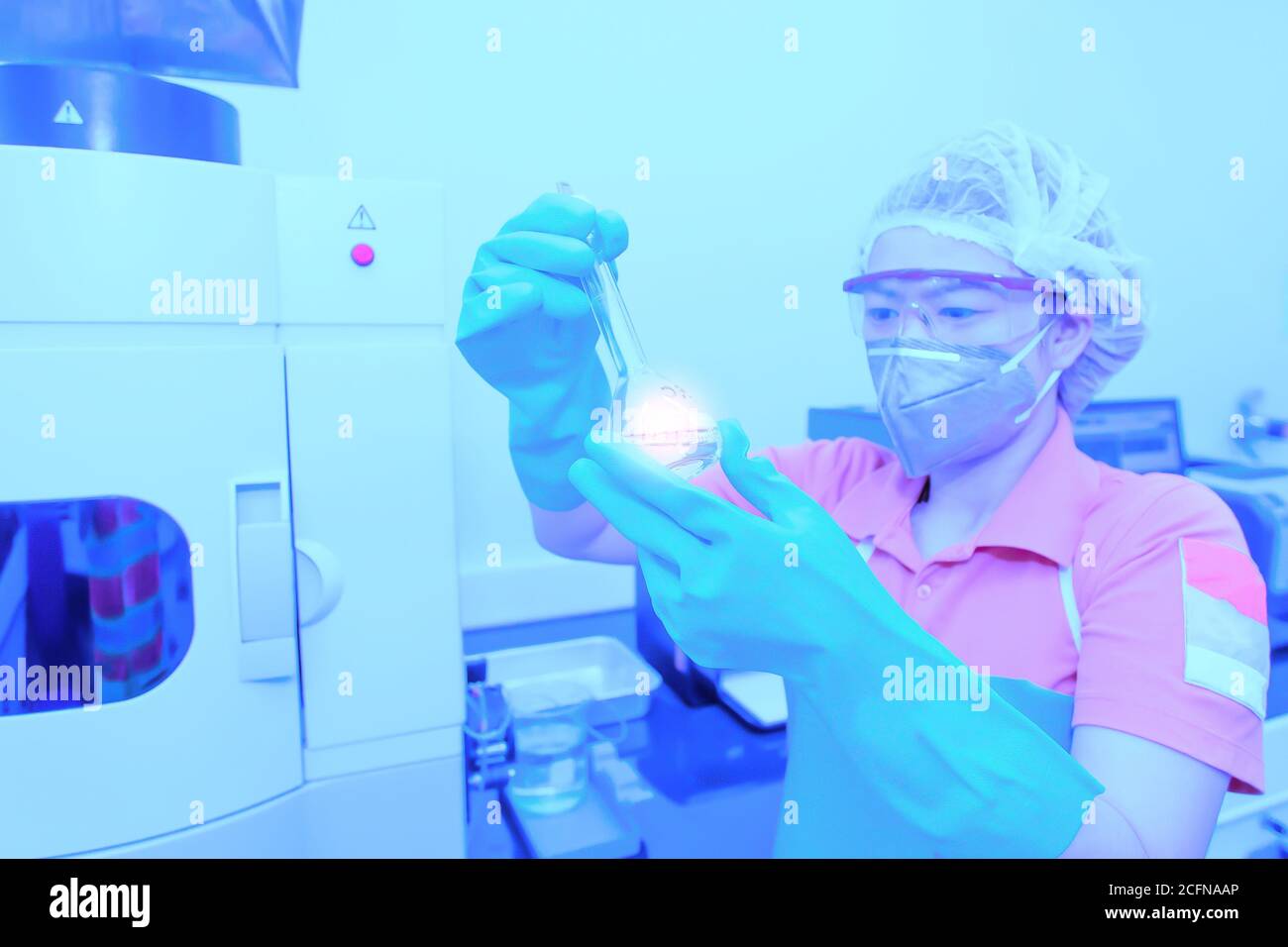 Une chercheuse asiatique portant un masque chirurgical tenant une fiole jaugée ou une éprouvette faisant des recherches en laboratoire. Mise au point douce sur la fl. Volumétrique Banque D'Images