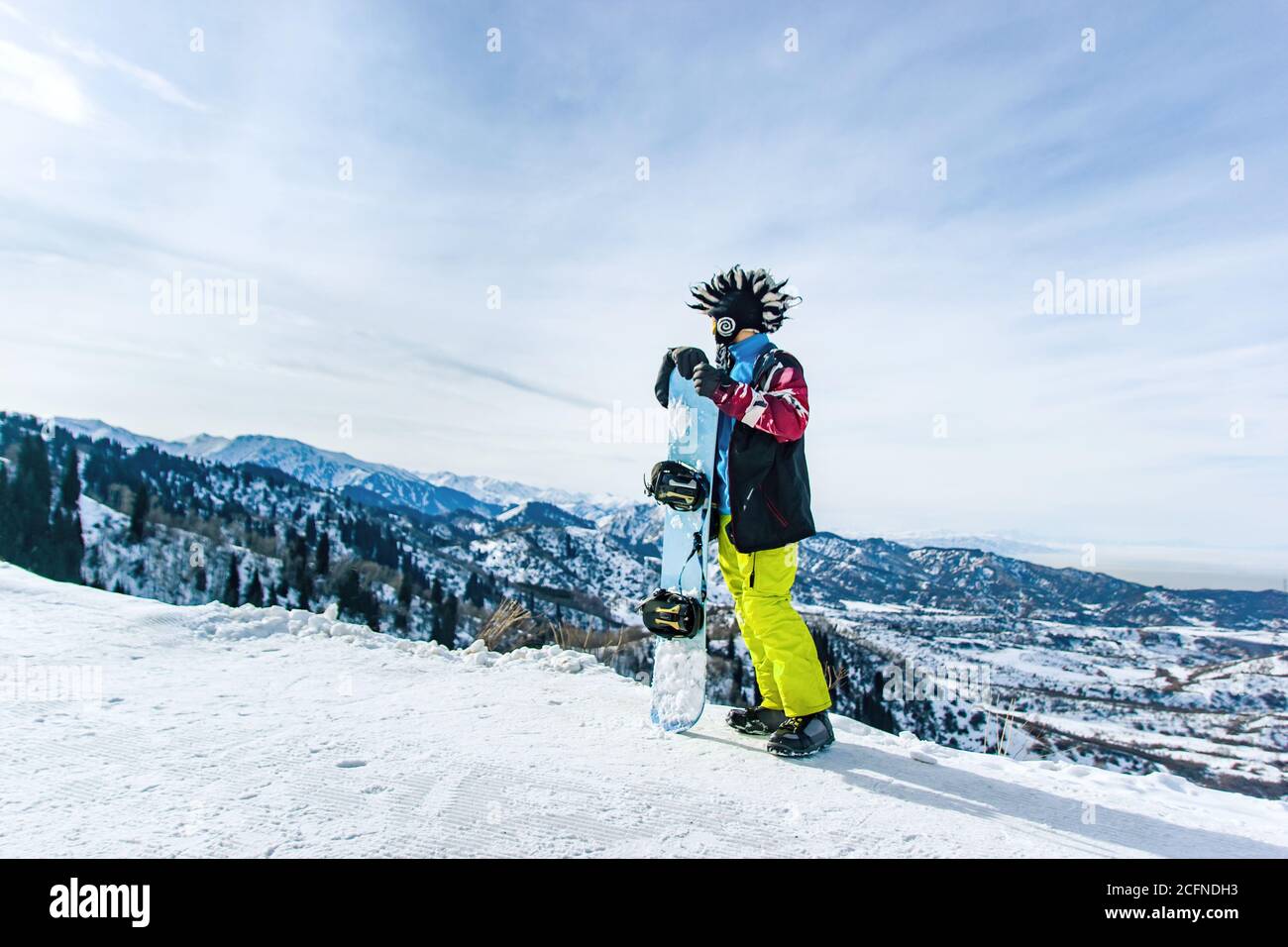 Bonhomme de neige à barbe dans un masque de ski avec des lunettes et un gros chapeau mohawk en fourrure sur fond de ciel et de montagnes enneigées d'hiver Banque D'Images