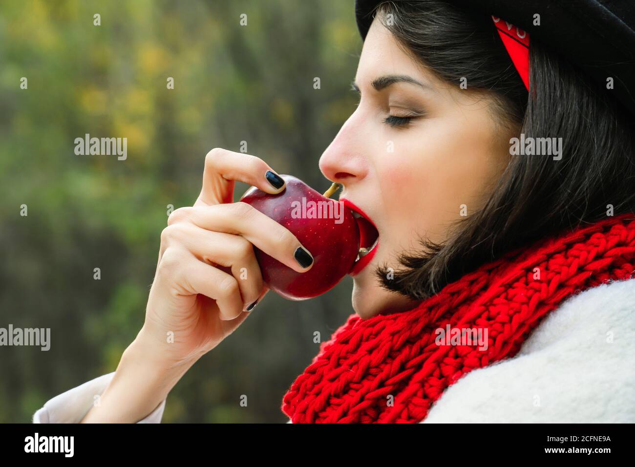 Belle femme mangeant une pomme rouge mûre. Foulard en crochet rouge et  chapeau noir, pique-nique extérieur Photo Stock - Alamy
