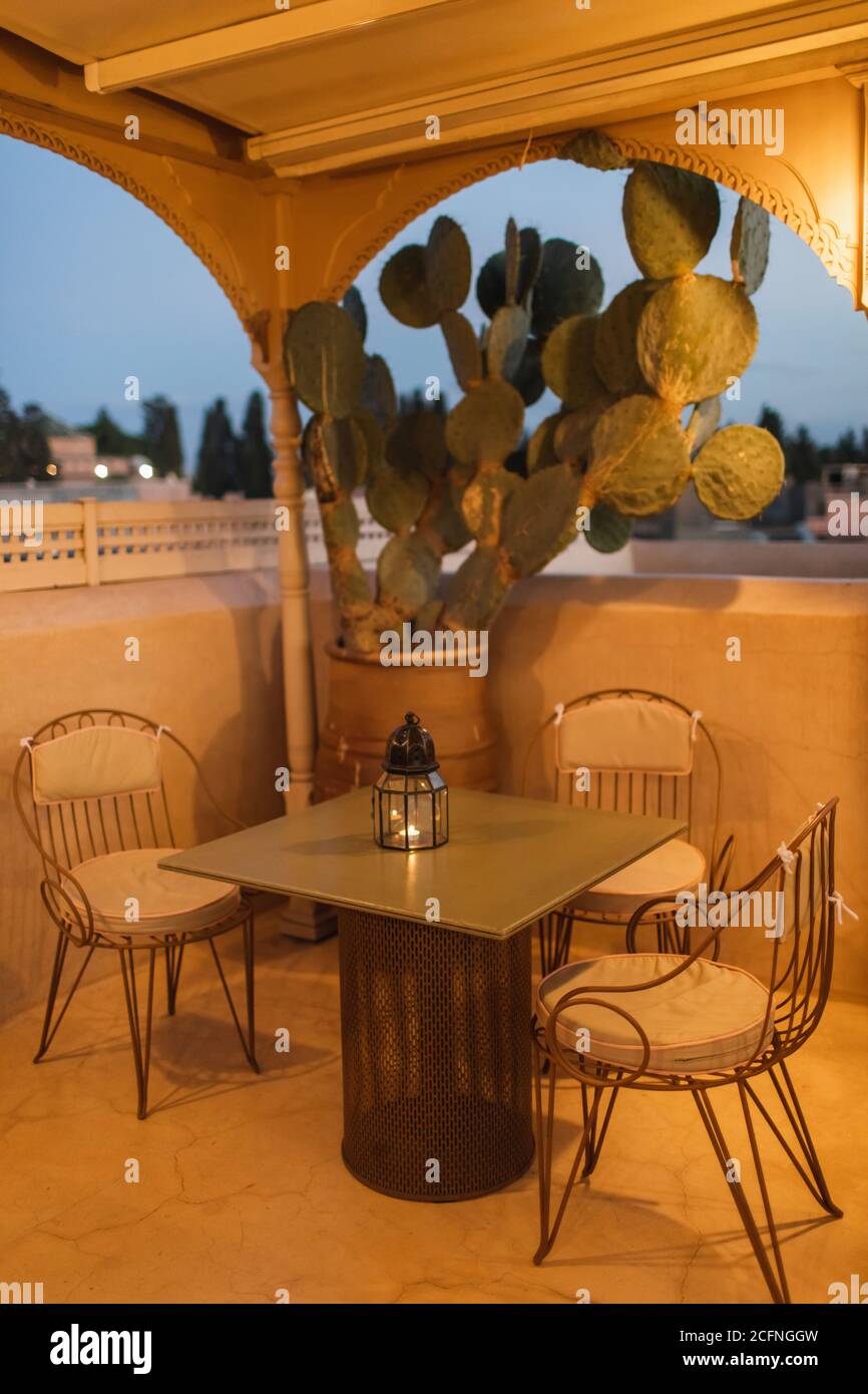 Table pour dîner romantique sur la terrasse sur le toit en soirée. Style marocain, lampes vintage, bougies, fleurs de cactus, crépuscule. Banque D'Images