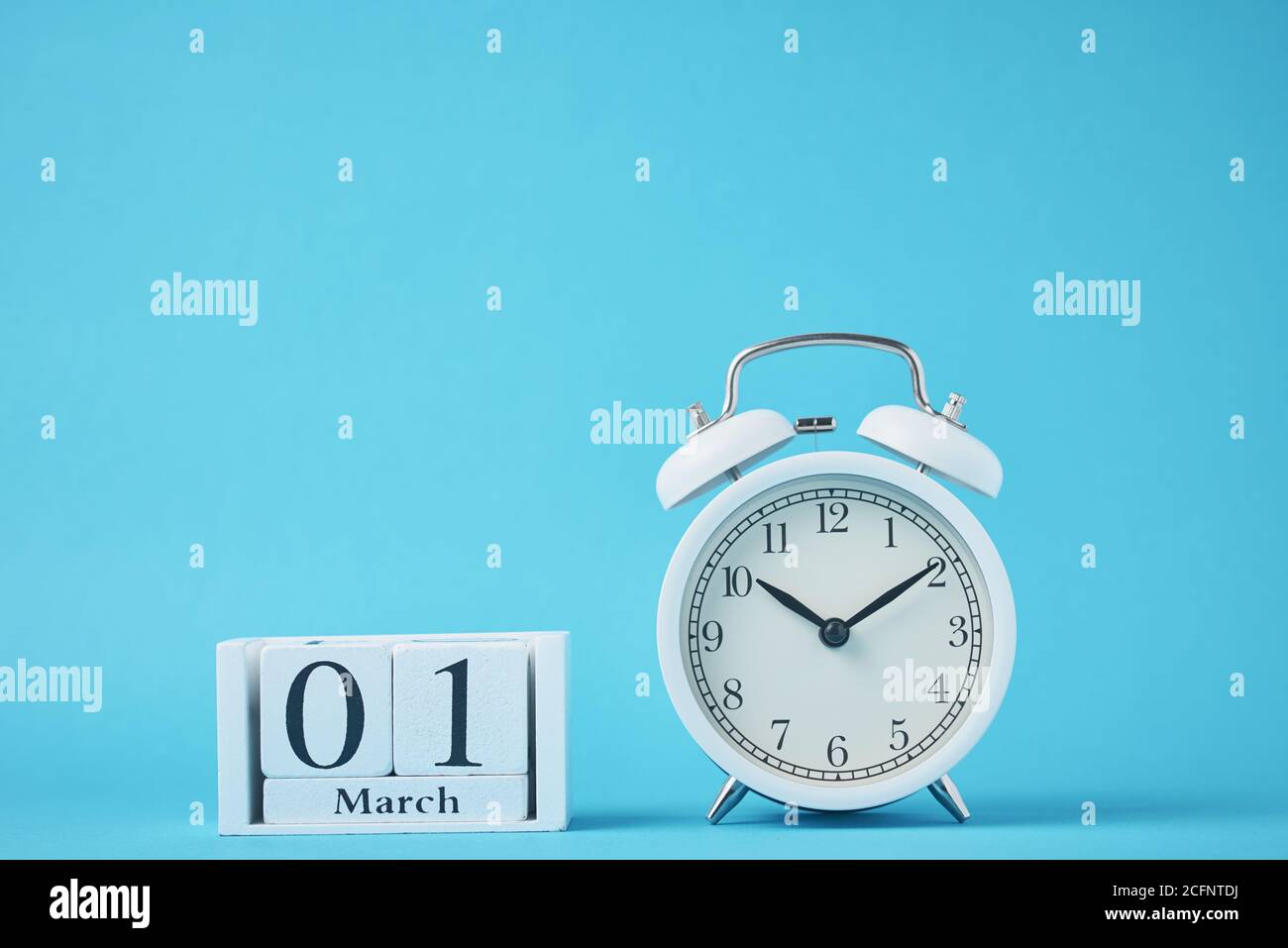 Réveil rétro blanc avec cloches et blocs calendrier en bois avec date du 1er mars sur fond bleu Banque D'Images