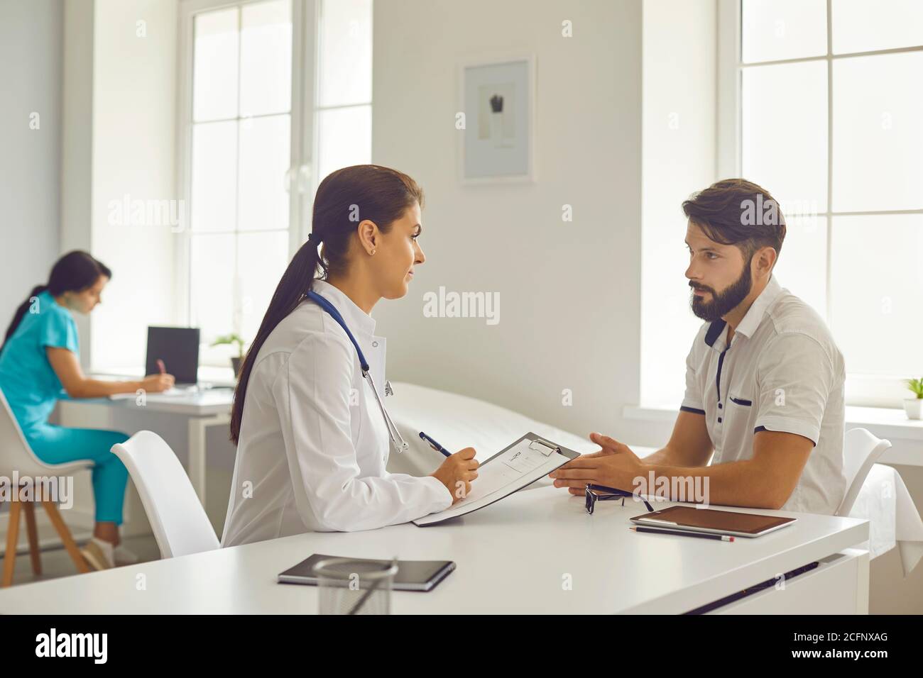 Clinique médicale. Femme souriante médecin assis et à l'écoute de l'homme parlant patient pendant la consultation Banque D'Images