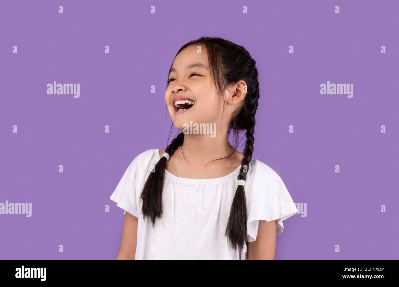 Joyeuse petite fille asiatique riant posant sur fond violet Banque D'Images