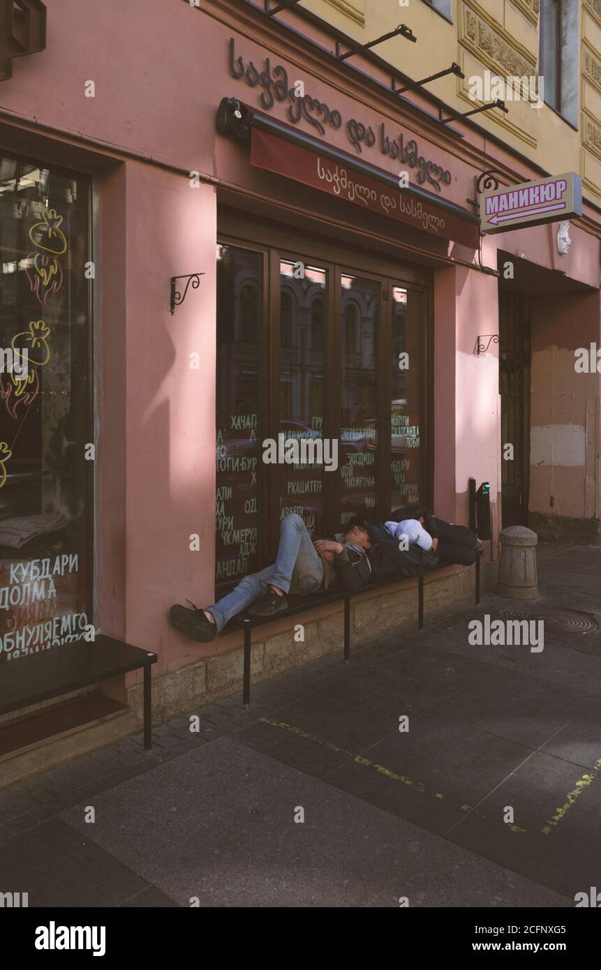 Saint-Pétersbourg, Russie - 21 août 2020 : les hommes sans domicile dorment sur un banc près d'un café sur le thème de la Géorgie. La fenêtre a des inscriptions en russe et en Geor Banque D'Images