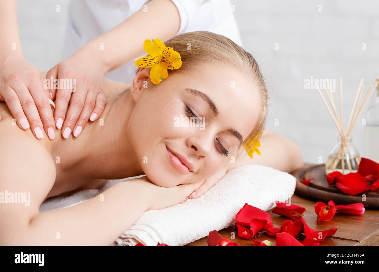 Détente et soins de beauté. Une fille souriante se trouve sur une table de massage aux pétales de fleurs Banque D'Images