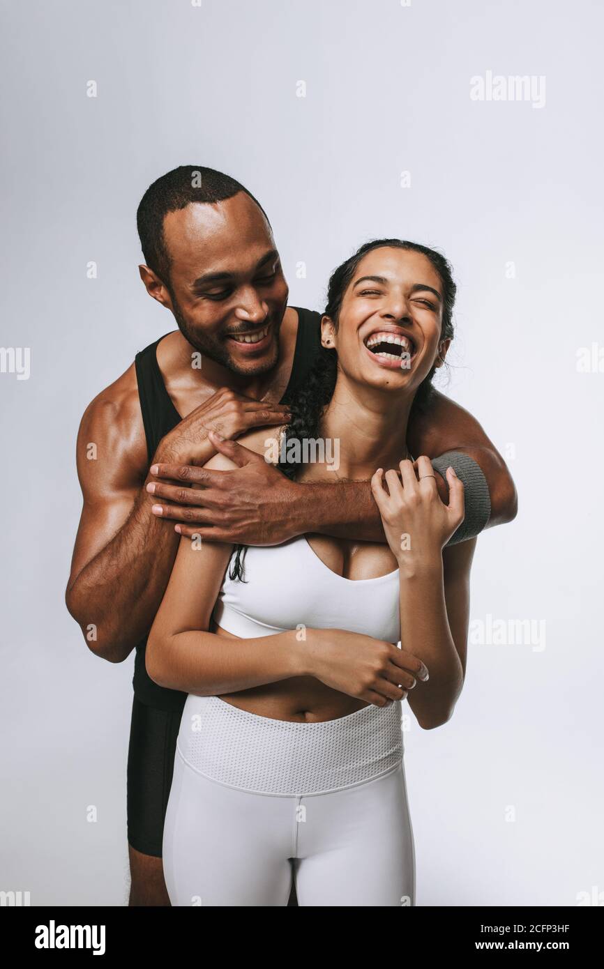 Souriant homme et femme en forme de vêtements s'amuser à la salle de gym. Homme musclé tenant la femme souriante de derrière dans les bras. Banque D'Images