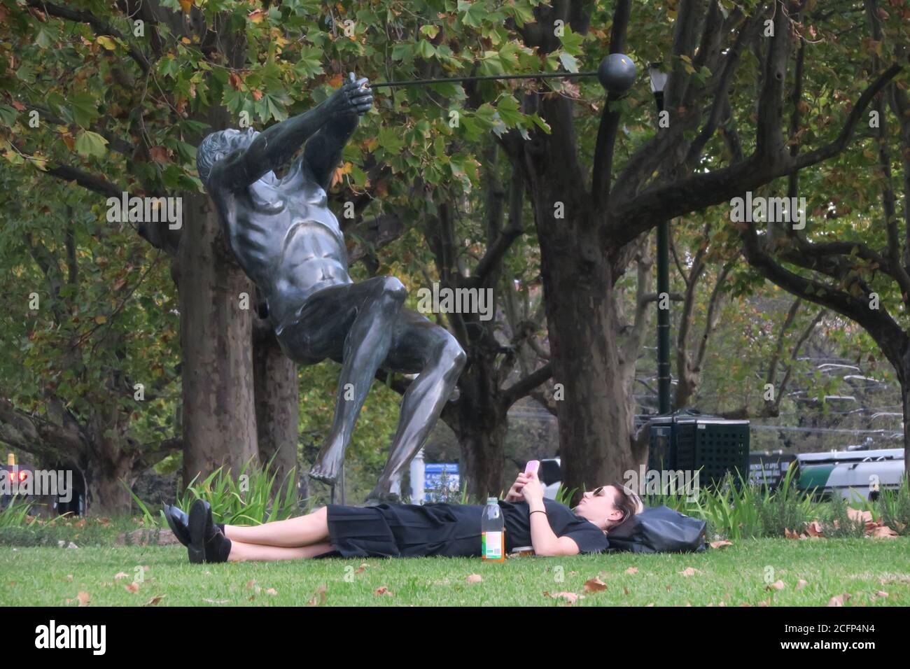 Melbourne Australie. Scènes de la vie quotidienne à Melbourne Australie . Lecture de votre téléphone en étant allongé dans un parc sous la « Sculpture marteau Thrower » Banque D'Images