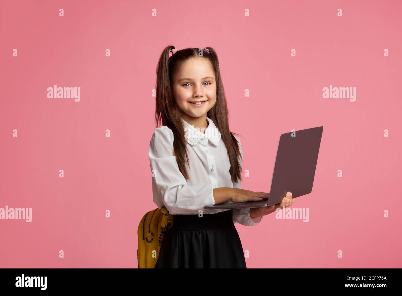 E-éducation. Une écolière souriante en uniforme avec sac à dos fonctionne sur un ordinateur portable Banque D'Images